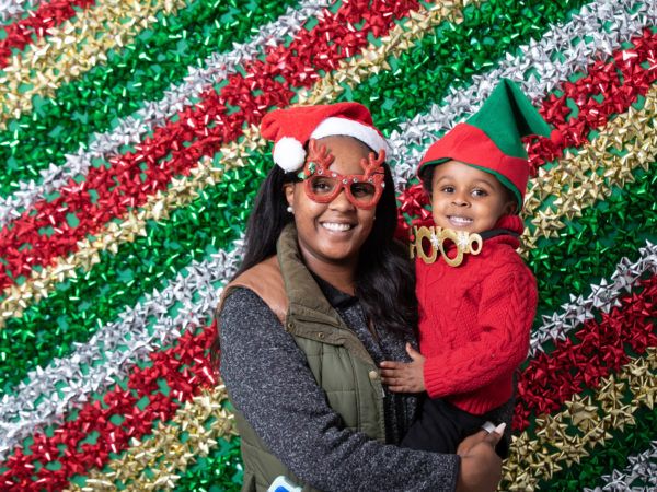 A mother holds her child in front of a backdrop of Christmas ribbons.