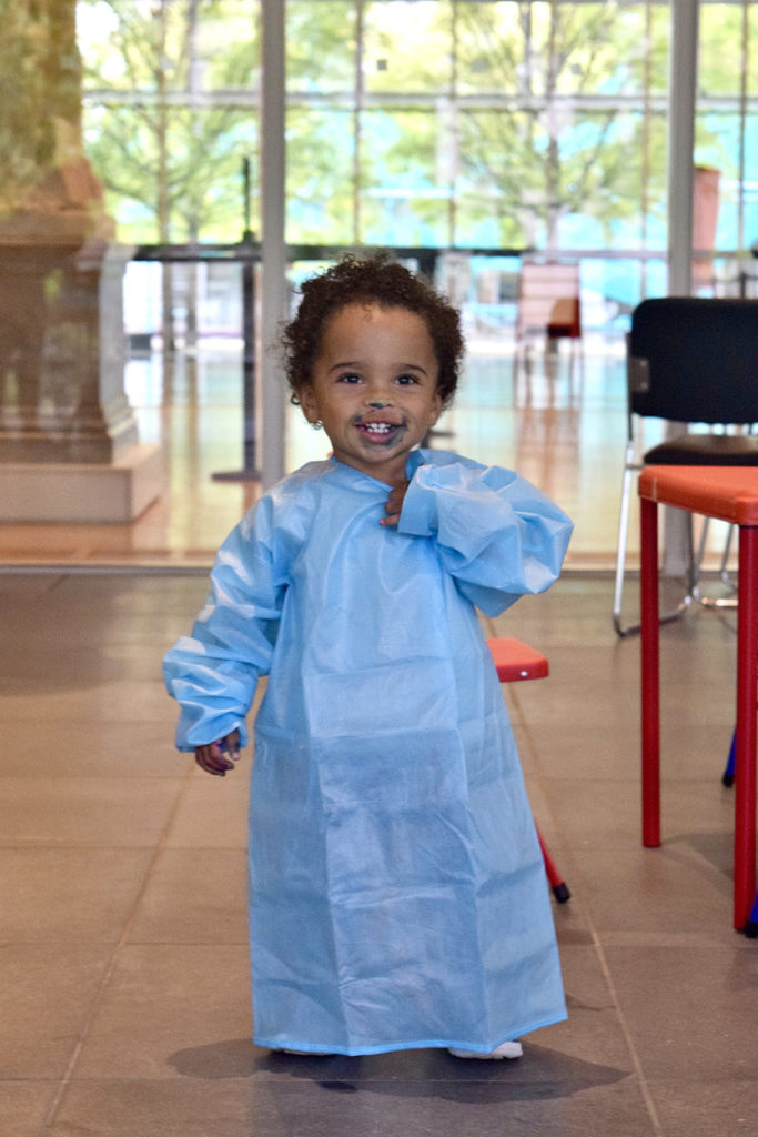 A toddler wears a smock.