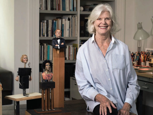 Susan Seydel Cofer sits in front of a bookshelf and a group of figurative sculptures.