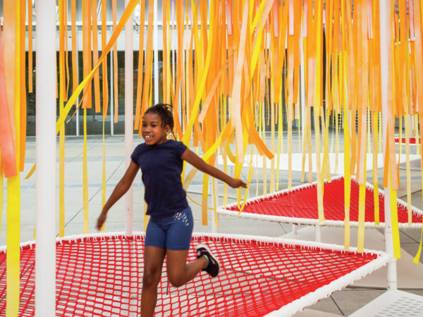 A child runs across red netting beneath long red, orange, and yellow strips.