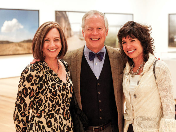 Three people pose together in a gallery of large photographs.