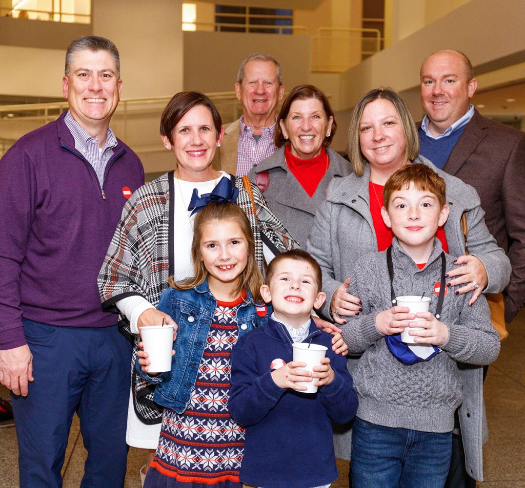 A group of people pose for the camera in the lobby; the three children at the front of the group hold paper cups.