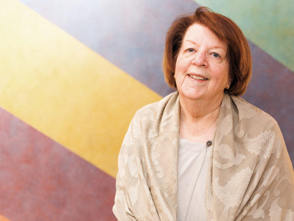 A woman with short red hair smiles at the camera in front of a cropped view of a colorful mural at the High Museum of Art.