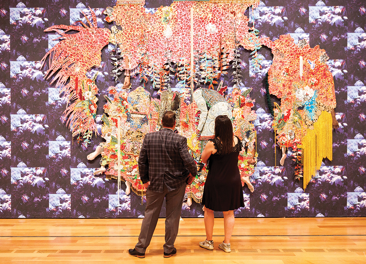 Two visitors examine a large, purple, decorative tapestry.