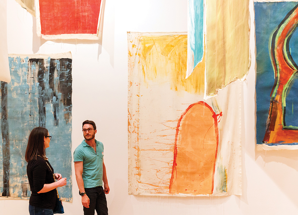 Two visitors stand near large paintings by Vivian Suter.
