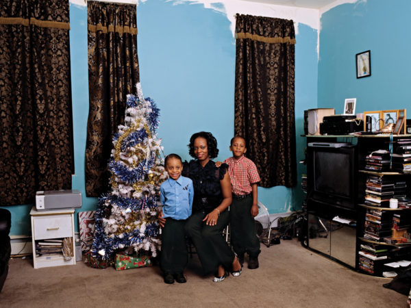 A picture of a woman with two children seated next to a blue, white, and gold decorated tree.
