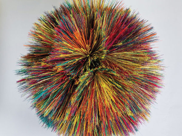 A colorful object in the shape of a large, fuzzy ball, made from broomcorn.
