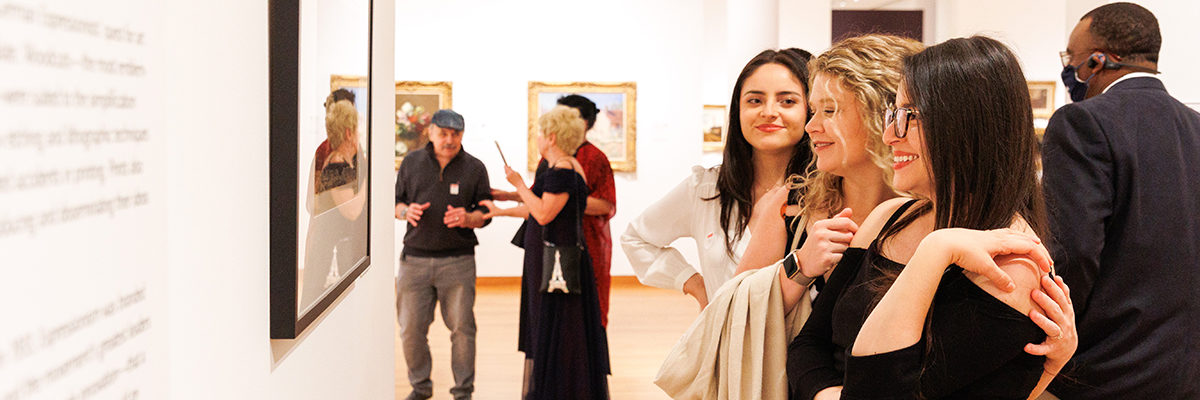 Three people stand together in front of a framed print in a gallery.