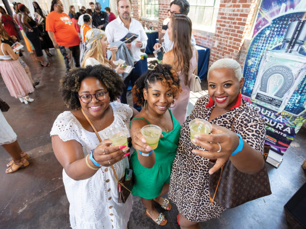 Three people pose, holding up drinks for the camera.
