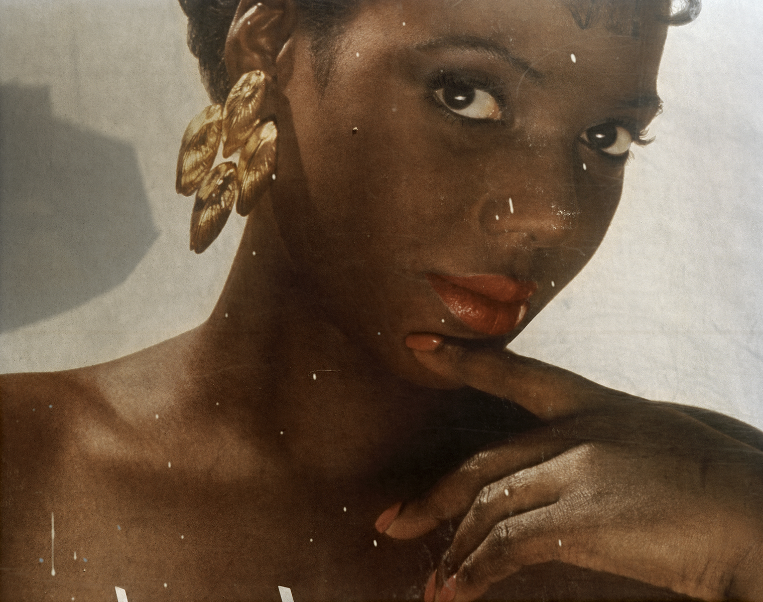 Photograph of an advertisement depicting a woman with large gold earring posing with a finger held to her chin.