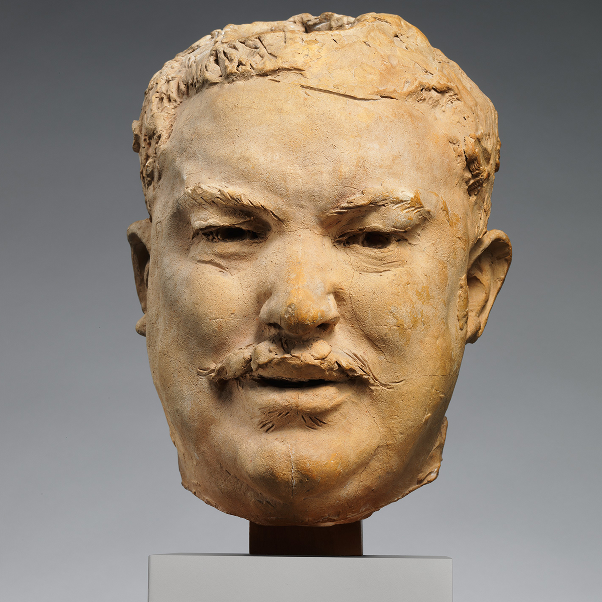Frontal view of the sculpted head of a man with a mustache.