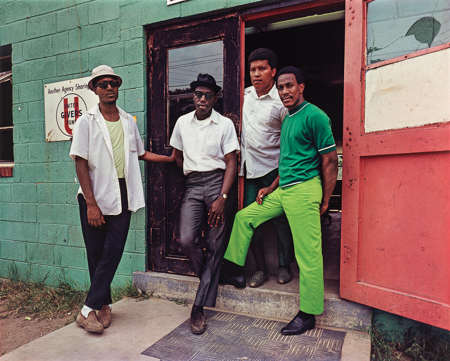 Four men stand in the doorway of a building, looking toward the camera.