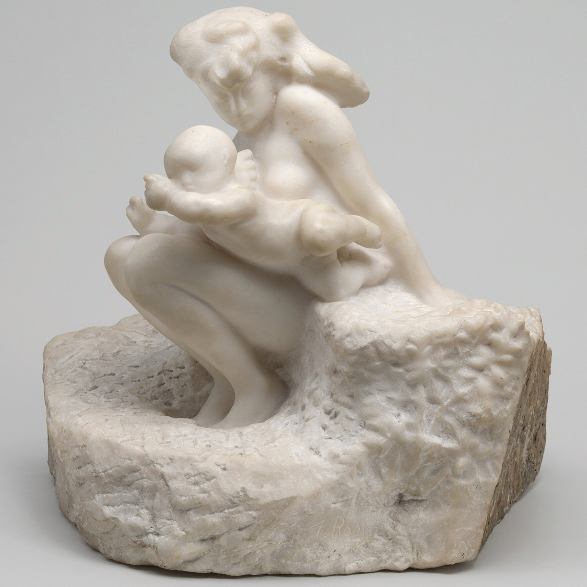 Seated woman holds an infant on her lap, carved in white marble.